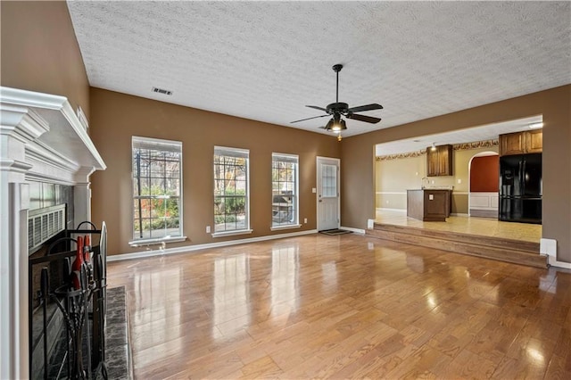 unfurnished living room with a fireplace, light wood-type flooring, ceiling fan, and a textured ceiling