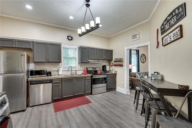 kitchen with ornamental molding, gray cabinets, a sink, light wood-style floors, and appliances with stainless steel finishes