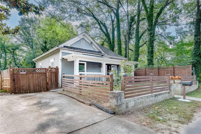 view of front of property with a porch, a gate, a fenced front yard, and a chimney