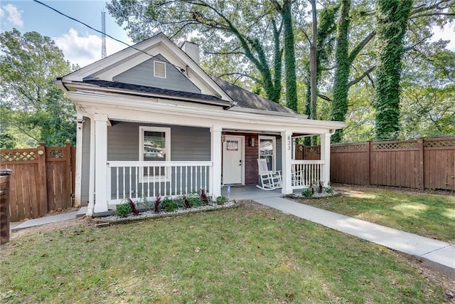 view of front facade featuring a chimney, a porch, a front lawn, and a fenced backyard