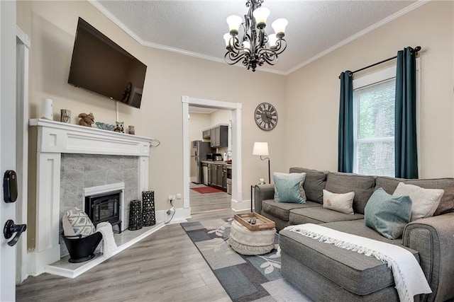 living area with wood finished floors, a tile fireplace, a textured ceiling, crown molding, and a notable chandelier