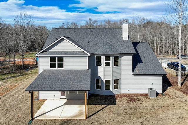 rear view of property with roof with shingles, central AC unit, a chimney, a patio area, and driveway