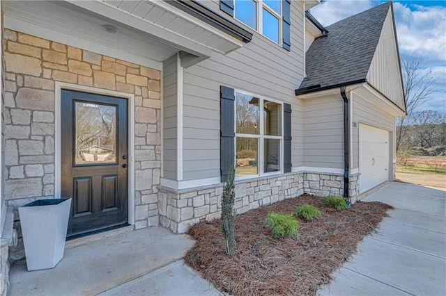 view of exterior entry with stone siding, a garage, concrete driveway, and roof with shingles