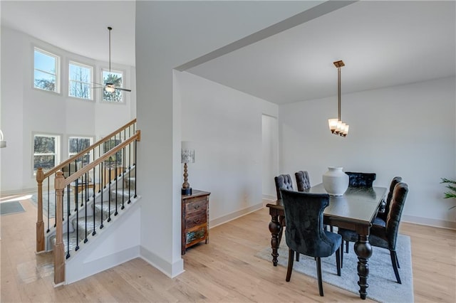 dining area with baseboards, light wood finished floors, stairs, a towering ceiling, and ceiling fan with notable chandelier