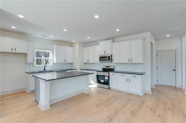 kitchen with a sink, a kitchen island, dark countertops, stainless steel appliances, and white cabinets