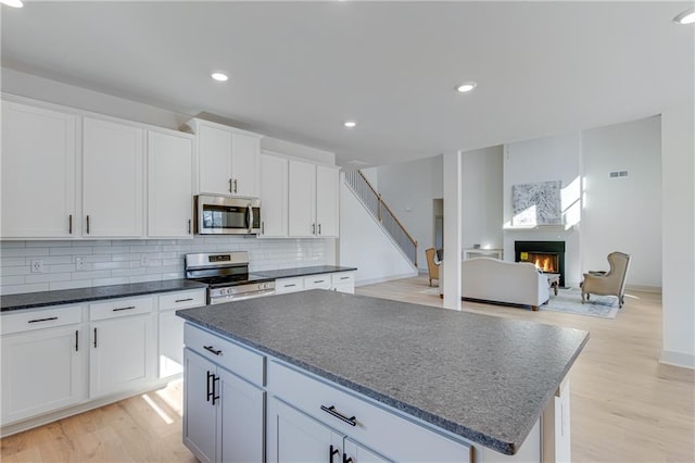 kitchen with a kitchen island, a lit fireplace, decorative backsplash, stainless steel appliances, and white cabinetry