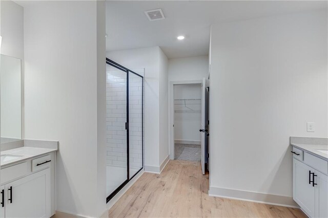 bathroom with wood finished floors, visible vents, two vanities, a shower stall, and a walk in closet