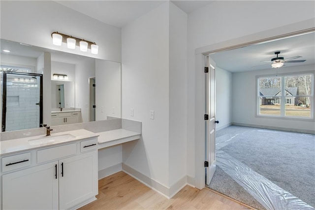 bathroom with vanity, a ceiling fan, wood finished floors, baseboards, and a stall shower