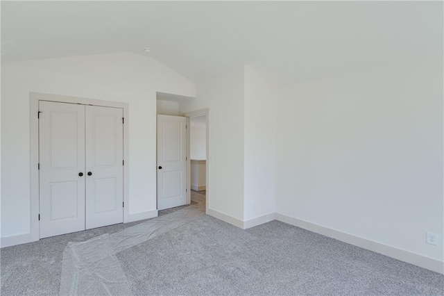 unfurnished bedroom with baseboards, lofted ceiling, carpet floors, and a closet