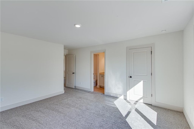 unfurnished bedroom with light carpet, recessed lighting, ensuite bathroom, and baseboards