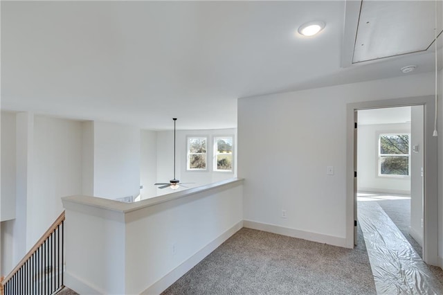 corridor with an upstairs landing, light colored carpet, attic access, and baseboards