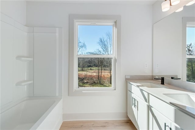 full bathroom featuring a sink, shower / tub combination, wood finished floors, double vanity, and baseboards