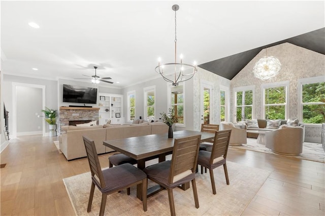 dining room with crown molding, a stone fireplace, lofted ceiling, and light hardwood / wood-style flooring