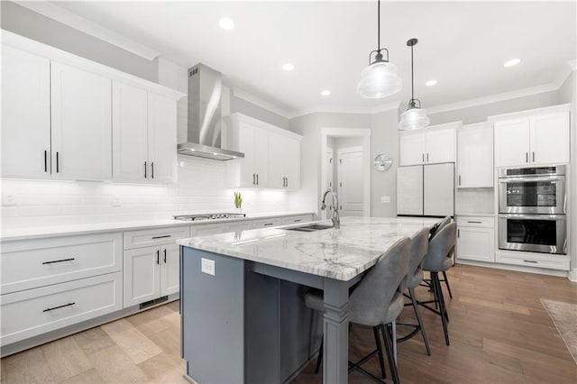 kitchen with a kitchen bar, a sink, appliances with stainless steel finishes, white cabinets, and wall chimney range hood