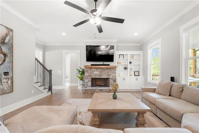 living area featuring a stone fireplace, stairs, light wood-style floors, and ornamental molding