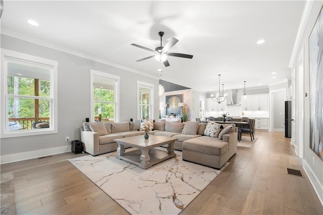 living room with ceiling fan with notable chandelier, ornamental molding, and light hardwood / wood-style floors