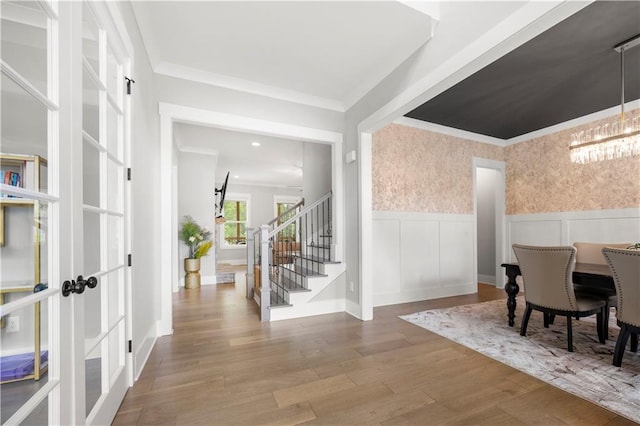 entrance foyer with wallpapered walls, crown molding, a wainscoted wall, stairs, and wood finished floors