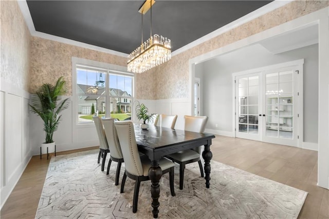 dining room featuring a wainscoted wall, wallpapered walls, wood finished floors, and ornamental molding