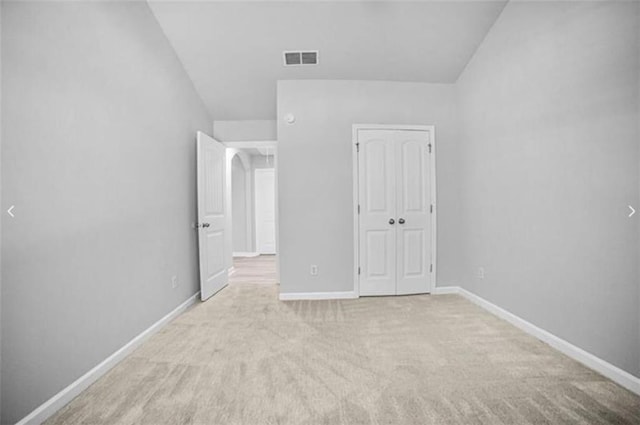 unfurnished bedroom with light colored carpet, vaulted ceiling, and a closet