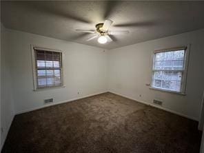 empty room with dark colored carpet, ceiling fan, and a wealth of natural light