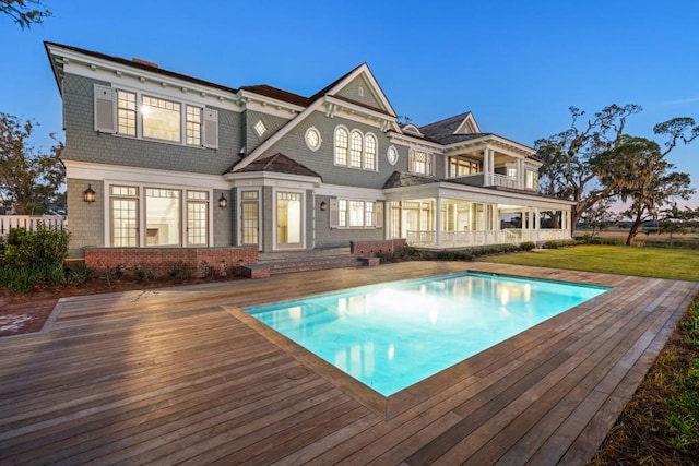 rear view of house with a swimming pool side deck, a balcony, and a lawn