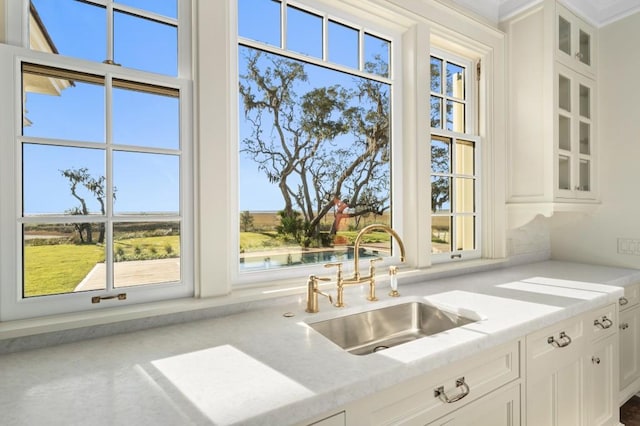 kitchen with light stone counters, concrete flooring, sink, a water view, and white cabinets