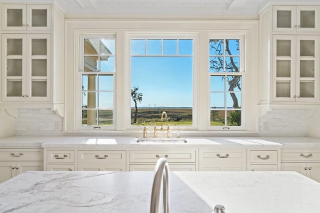 kitchen featuring light stone countertops, tasteful backsplash, white cabinetry, and sink