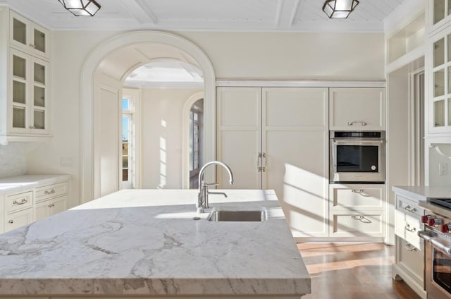 kitchen featuring hardwood / wood-style floors, sink, an island with sink, light stone counters, and stainless steel appliances