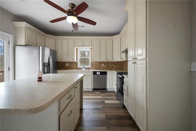 kitchen featuring tasteful backsplash, appliances with stainless steel finishes, a center island, light countertops, and a sink