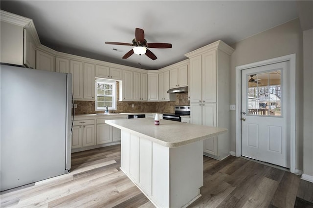 kitchen featuring under cabinet range hood, stainless steel appliances, a kitchen island, light wood-style floors, and light countertops