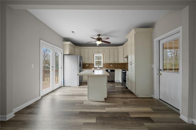 kitchen with cream cabinets, a kitchen island, light countertops, appliances with stainless steel finishes, and backsplash