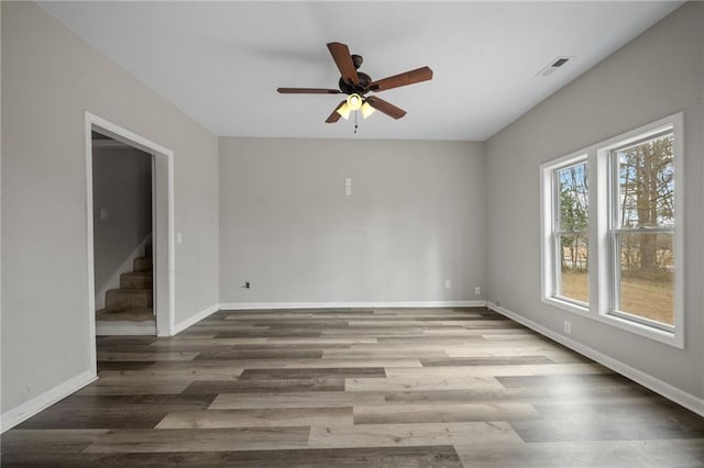 empty room featuring stairs, visible vents, baseboards, and wood finished floors