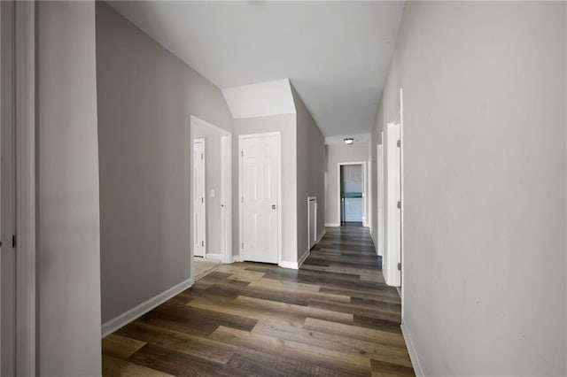 hallway featuring dark wood-style floors, lofted ceiling, and baseboards