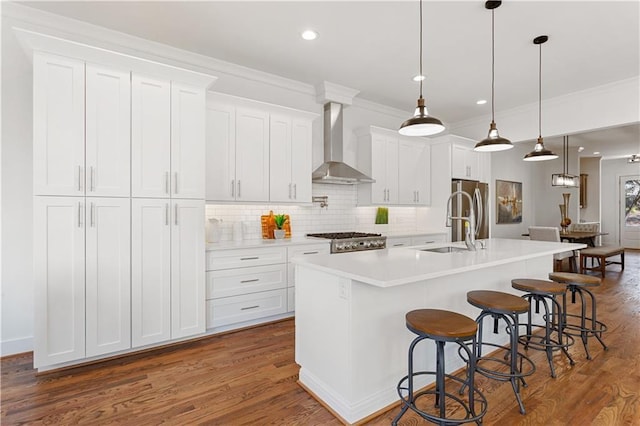 kitchen featuring wall chimney exhaust hood, white cabinetry, decorative light fixtures, a kitchen breakfast bar, and an island with sink