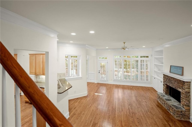 unfurnished living room featuring built in features, a fireplace, light wood finished floors, ornamental molding, and baseboards