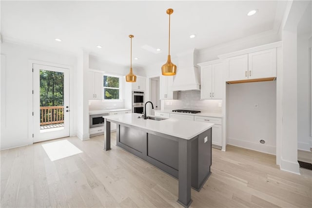 kitchen with white cabinets, sink, a center island with sink, decorative light fixtures, and custom range hood