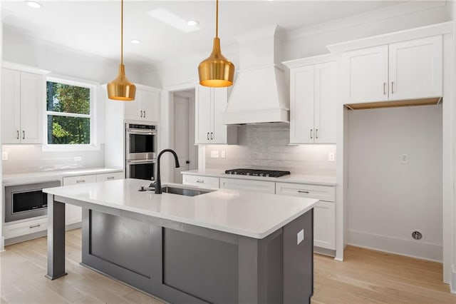 kitchen featuring white cabinets, hanging light fixtures, sink, a kitchen island with sink, and appliances with stainless steel finishes