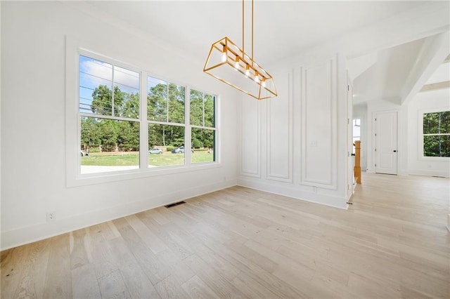 unfurnished dining area featuring light hardwood / wood-style floors, an inviting chandelier, and a wealth of natural light