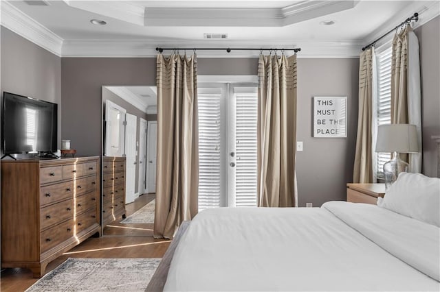 bedroom featuring ornamental molding, wood-type flooring, a tray ceiling, and multiple windows