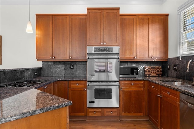 kitchen featuring appliances with stainless steel finishes, sink, hanging light fixtures, and dark stone counters