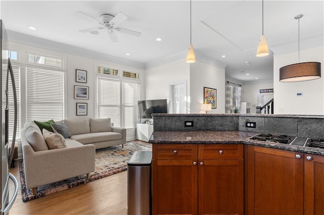 kitchen featuring hanging light fixtures, appliances with stainless steel finishes, ceiling fan, dark stone counters, and light hardwood / wood-style floors