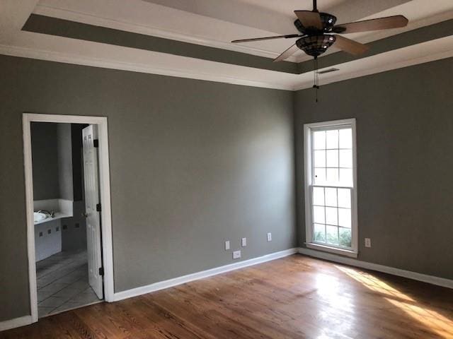 unfurnished room featuring a raised ceiling, ceiling fan, dark hardwood / wood-style flooring, and ornamental molding