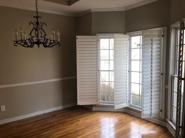 empty room with hardwood / wood-style floors, a chandelier, and ornamental molding