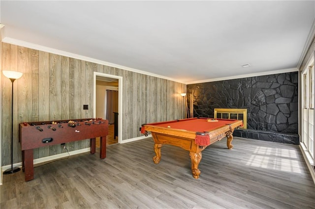 recreation room with pool table, a stone fireplace, wood finished floors, and ornamental molding