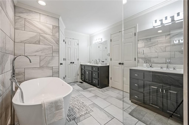 full bathroom featuring a freestanding bath, ornamental molding, two vanities, marble finish floor, and tile walls