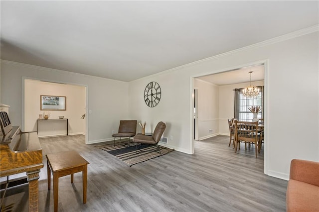 living area featuring a notable chandelier, wood finished floors, baseboards, and ornamental molding