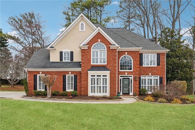 view of front of home with stucco siding, roof with shingles, a front lawn, and brick siding