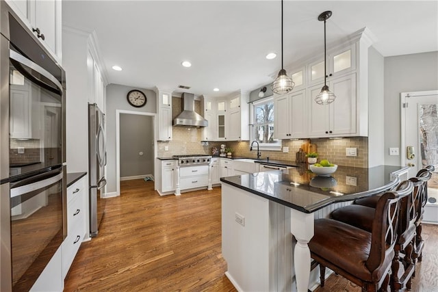 kitchen featuring appliances with stainless steel finishes, dark countertops, a peninsula, and wall chimney exhaust hood