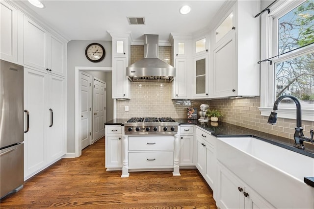 kitchen featuring stainless steel appliances, visible vents, white cabinets, a sink, and wall chimney exhaust hood