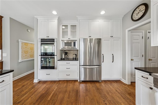 kitchen with tasteful backsplash, white cabinets, dark countertops, appliances with stainless steel finishes, and dark wood-style flooring